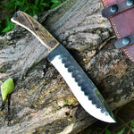 Camping knife with antler horn handle and leather sheath on a rustic wooden background